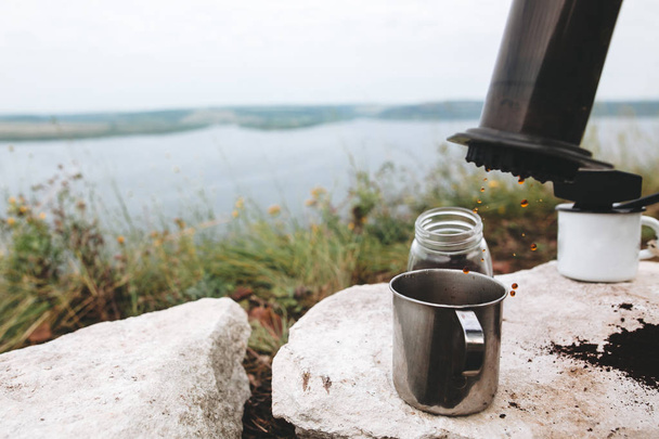 Coffee drops from aeropress on metal mug on cliff at lake, brewi - Foto, Bild