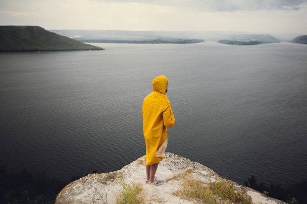 Hipster viajero en impermeable amarillo de pie en el acantilado y lookin
 - Foto, imagen