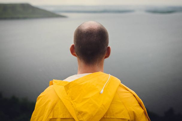 Hombre con impermeable amarillo viajando por el acantilado y mirando el lago en
 - Foto, imagen