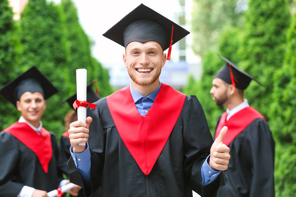 Male student in bachelor robe and with diploma outdoors - Foto, imagen