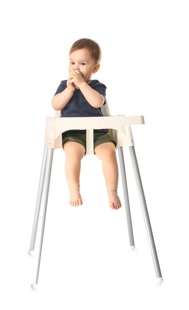 Cute little boy with nibbler sitting in high chair against white background - 写真・画像
