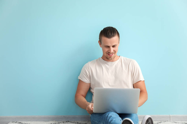 Blogueur masculin avec ordinateur portable assis près du mur de couleur
 - Photo, image