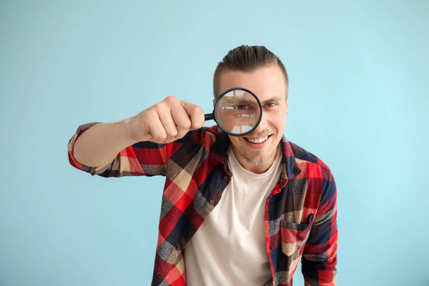 Young man with magnifying glass on color background - 写真・画像