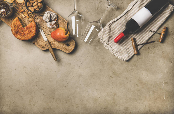 Wine and snack set. Flat-lay of wine bottle with blank label, vintage corkscrews, wineglasses, cheese and appetizers on board over grey concrete background, top view, copy space. Party food concept - Foto, Bild