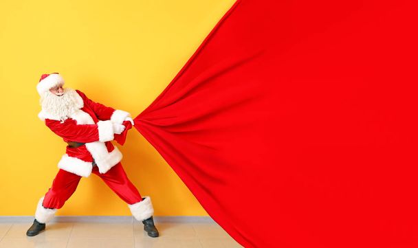 Portret van de Kerstman trekken grote tas tegen kleur muur - Foto, afbeelding