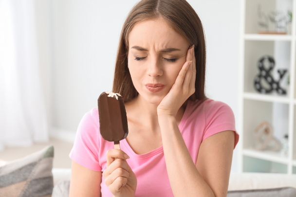 Νεαρή γυναίκα με ευαίσθητα δόντια και κρύο παγωτό στο σπίτι - Φωτογραφία, εικόνα