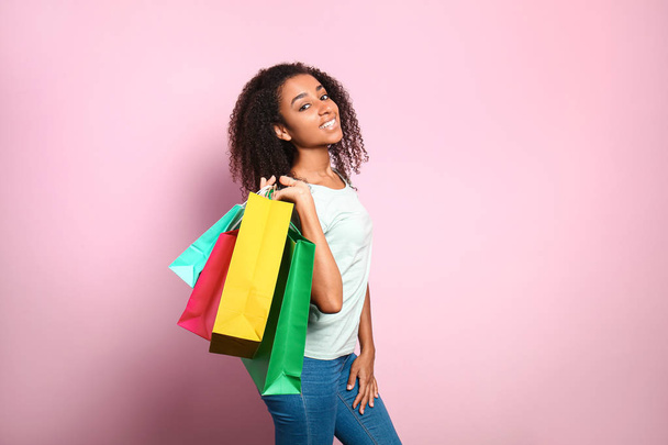Portrait of happy African-American woman with shopping bags on color background - Foto, Imagen