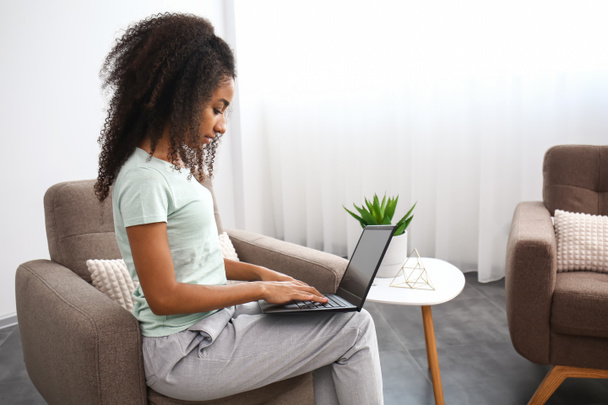 Bella donna afroamericana con computer portatile seduto in poltrona a casa
 - Foto, immagini