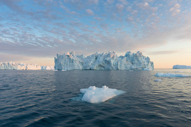 Φύση και τοπία της Γροιλανδίας ή της Ανταρκτικής. Ταξιδέψτε στο πλοίο μεταξύ παγετώνων. Μελέτη ενός φαινομένου της υπερθέρμανσης του πλανήτη Παγόβουνα και παγόβουνα ασυνήθιστων μορφών και χρωμάτων Όμορφος μεσονύκτιος ήλιος στο πλοίο  - Φωτογραφία, εικόνα