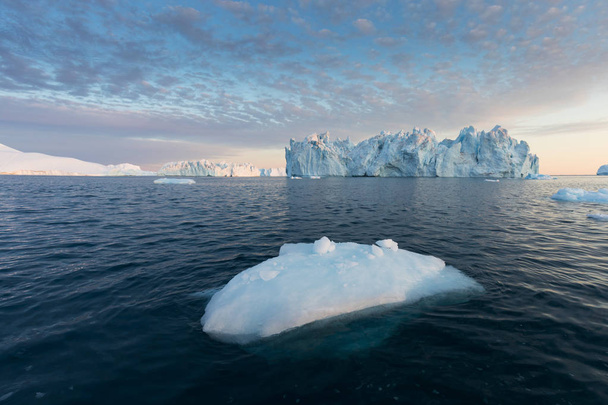 Grönlannin tai Etelämantereen luonto ja maisemat. Matkustaa aluksella jäällä. Ilmaston lämpenemisen ilmiön tutkiminen Epätavallisten muotojen ja värien jäät ja jäävuoret Kaunis keskiyön aurinko laivalla
  - Valokuva, kuva