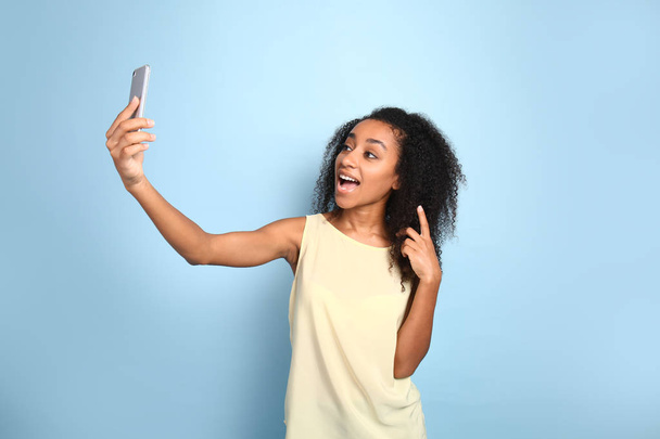 Portrait of happy African-American woman taking selfie on color background - Photo, image