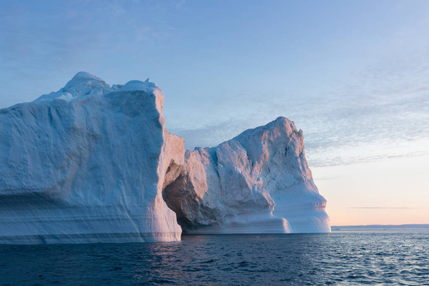 グリーンランドや南極の自然や風景。氷の間で船の旅。地球温暖化現象の研究異常な形と色の氷と氷山船に乗って美しい真夜中の太陽  - 写真・画像