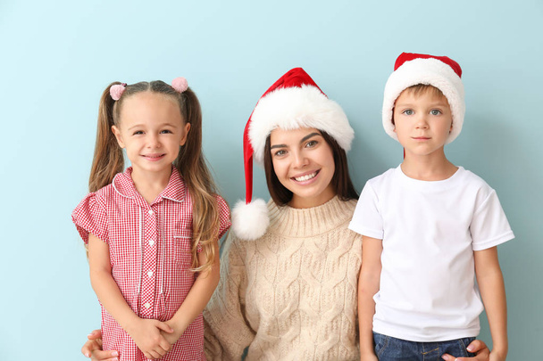 Kleine kinderen en hun moeder in Santa hoeden op kleur achtergrond - Foto, afbeelding