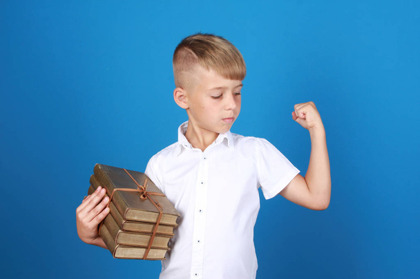 Serious proud cute boy wearing school uniform, making power gesture and showing bicep. Schoolboy isolated on blue background. Back to school, education, knowledge concept - Фото, изображение