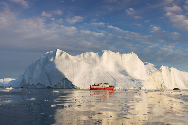 氷山の中の小さなボート真夜中の太陽イルリサット、グリーンランドの間にディスコ湾の氷河の浮遊氷山の間でヨットクルージング。地球温暖化氷と氷山現象の研究 - 写真・画像