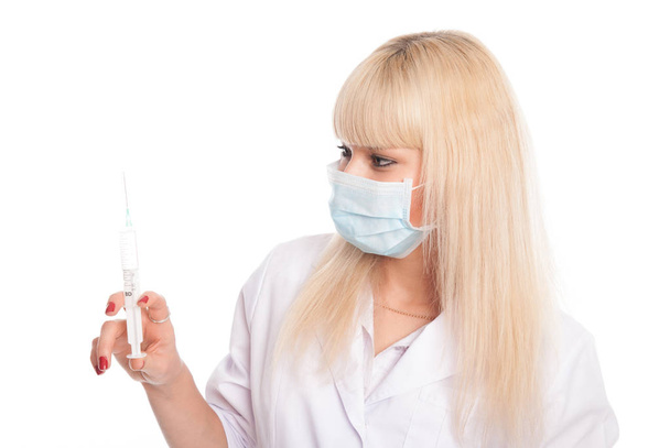 Close-up of a young blonde nurse in a mask looking at a syringe. - Foto, Imagem