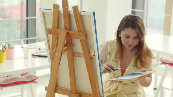 彼女のワークショップで働く女性アーティストは、美しい絵を作成し、カラフルな油で絵を描きます。キャンバスに描く女性画家 - 映像、動画