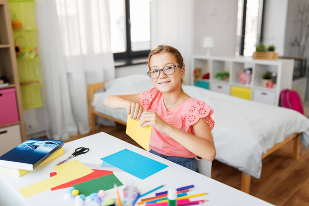 girl with color paper sitting at table at home - Photo, Image