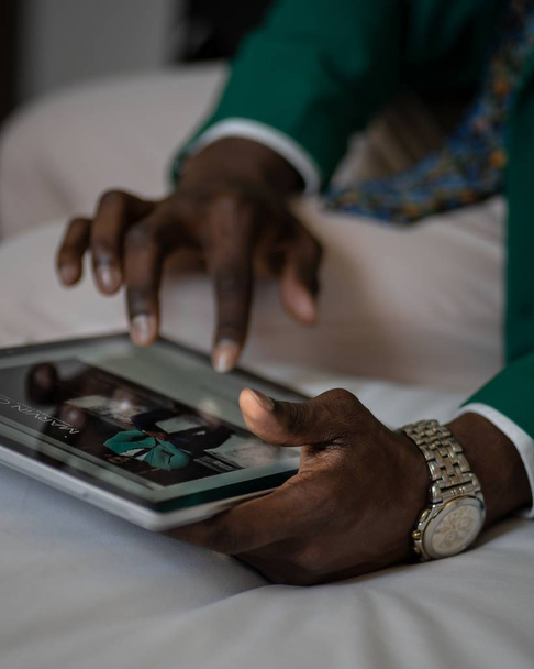 selective closeup shot of an African person wearing green suit and gray wristwatch using a tablet - Fotoğraf, Görsel