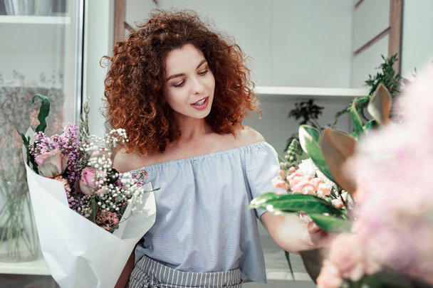 Zainteresowany kręcone włosy młoda dama dotyka łodygi świeżych kwiatów - Zdjęcie, obraz