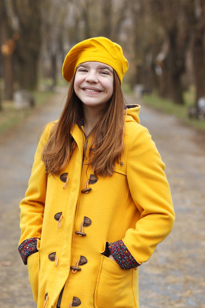 schöne Teenager-Mädchen in einem gelben Mantel und Baskenmütze Porträt  - Foto, Bild