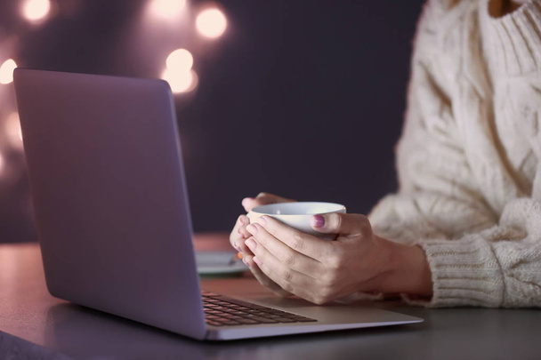Жінка з ноутбуком і чашкою кави працює за столом ввечері
 - Фото, зображення