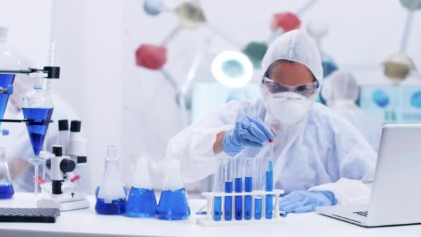 Female scientist taking samples of blue liquid from different test tubes using a pipette - Metraje, vídeo