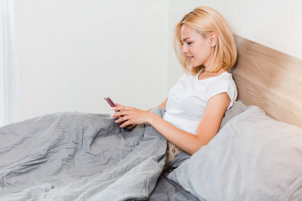 Beautiful young woman using phone in bed - 写真・画像
