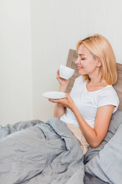Woman sitting on bed drinking coffee - Foto, afbeelding