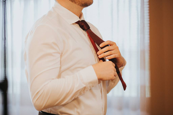 Male fixing his red tie before the wedding ceremony begins - Photo, Image