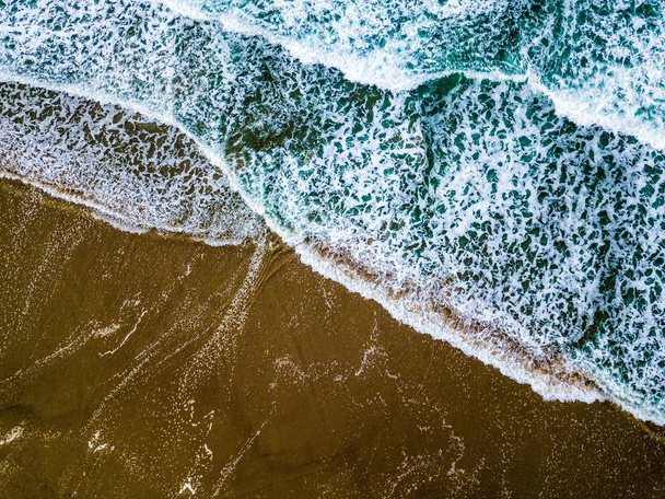 Wide shot of blue sea waves on a sandy seashore - 写真・画像