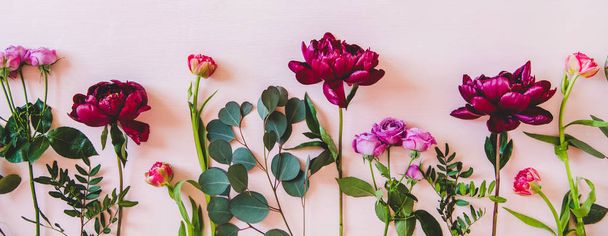 Summer flowers flat-lay. Purple peonies, pink roses and tulips and green branches over pastel pink background, top view, copy space, wide composition. Flower texture, wallpaper, background - Фото, изображение