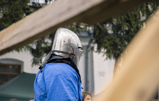 Ridder in stalen helm en middeleeuwse doek in ongerichte houten hek frame klaar voor gevechten op middelbare leeftijd historisch Festival  - Foto, afbeelding