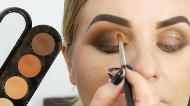 Professional master makeup artist applies beige eyeshadow palette with special brush on model eye at beauty salon close up view - Footage, Video