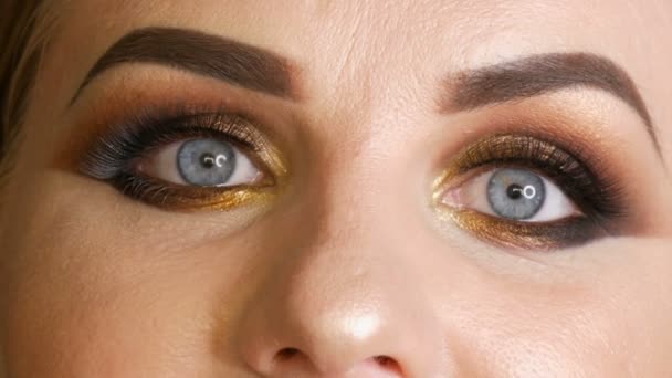 Modelo de mulher gorda bonita com maquiagem dourada, olhos fumegantes batom vermelho escuro pestanas falsas e olhos azuis posando em um fundo preto no estúdio. Cara vista de perto
 - Filmagem, Vídeo