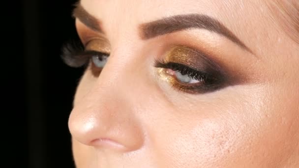 Mooie vette vrouw model met gouden make-up, rokerige ogen donkerrode lippenstift valse wimpers en blauwe ogen poseren op een zwarte achtergrond in de Studio. Gezicht close-up bekijken - Video