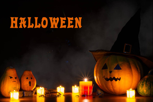Halloween background with the lettering "Halloween ". Pumpkin in a black hat in the light of burning candles. Pumpkins, mice, spiders, toad against a dark background. - Photo, Image