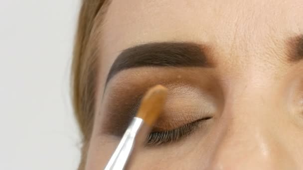Profesjonalny mistrz makijaż artysta stosuje beżowe Eyeshadow ze specjalnym pędzlem na oko modelu w salonie piękności z bliska widok - Materiał filmowy, wideo