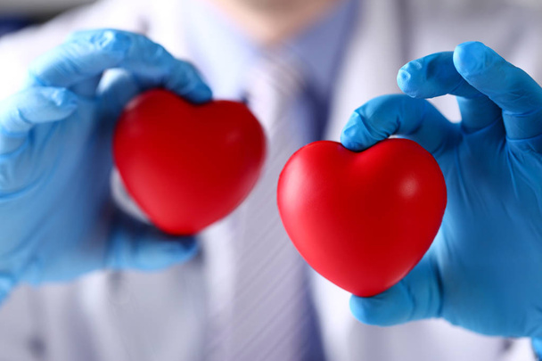 Chirurg w niebieskich rękawicach ukazujących dwie czerwone zabawki serca - Zdjęcie, obraz