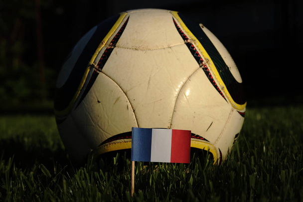 Campeonato de fútbol 2022. Euro 2020. Bandera nacional de Francia en palo de madera en hierba con pelota de fútbol típica en el fondo. Autoestima. Tricolor que significa todo para los franceses
 - Foto, Imagen
