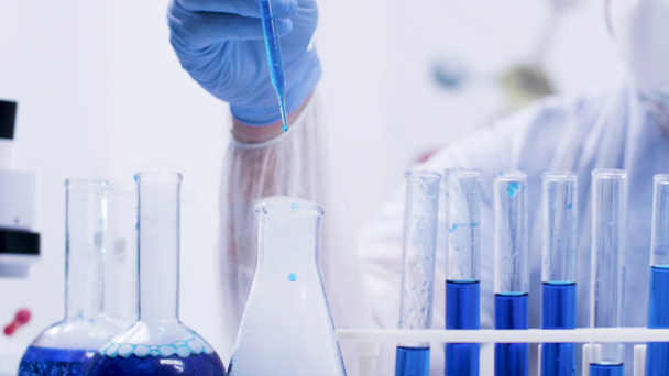 Científica química femenina en un moderno laboratorio que vierte reactivo con pipeta de tubos de ensayo con líquido azul
 - Imágenes, Vídeo