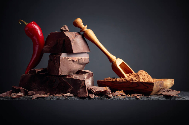 Chocolate negro con pimiento rojo y plato de madera con cacao en polvo
 - Foto, imagen