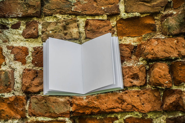 Open white book is on red brick wall. abandoned brick wall background. empty blank - copy space for inscription.  - Foto, afbeelding