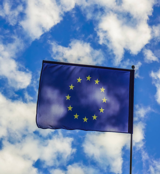 Bandeira da União Europeia acenando ao vento no mastro da bandeira contra o céu azul no dia ensolarado, close-up
 - Foto, Imagem