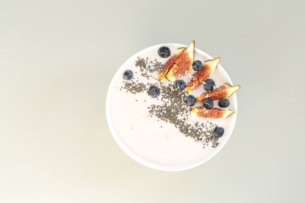 Healthy breakfast berry smoothie bowl topped with figs, coconut and chia seeds. Top view of a smoothie bowl with fresh ripe blueberry, figs, yogurt, coconut and chia. The concept of healthy eating and lifestyle.  - Zdjęcie, obraz