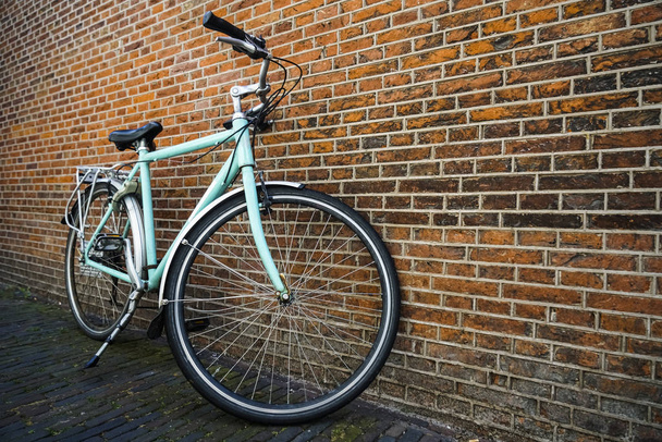 Blue vintage city bicycle without basket standing near red brick wall. - Foto, afbeelding