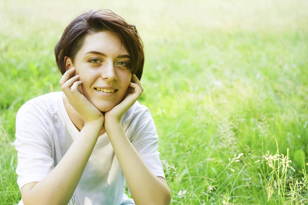 Beautiful portrait of pensive young short haired girl on blurred green grass meadow background, closeup. empty copy space for inscription. happy smiley face. - Foto, Imagen