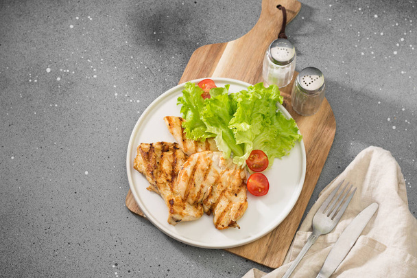Grilled chicken fillet with greens on a white plate. Gray background - Фото, зображення