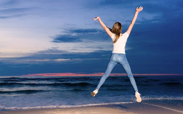 tiener meisje springen op het strand in de schemering tijd - Foto, afbeelding