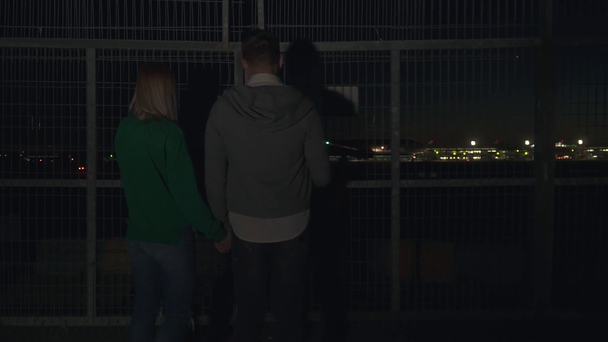 Молодий хлопець і дівчина спостерігають, як літак злітає вночі. Молода пара тримає руки і дивиться, як літак рухається на злітно-посадкову смугу
. - Кадри, відео
